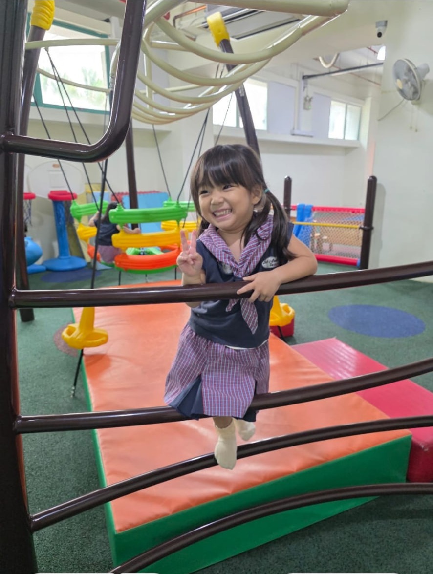 A smiling girl playing on the indoor playground climbing frame