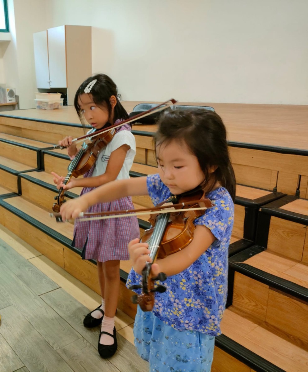 Two children practising the violin on stage