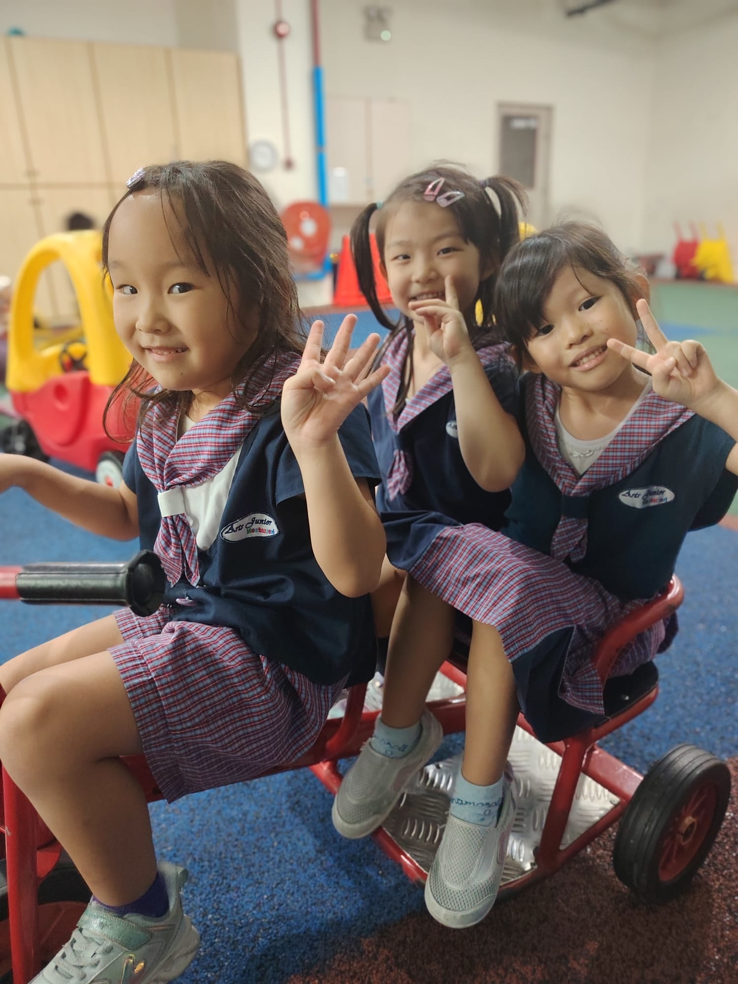 Three Arts Junior friends smiling together on a tricycle
