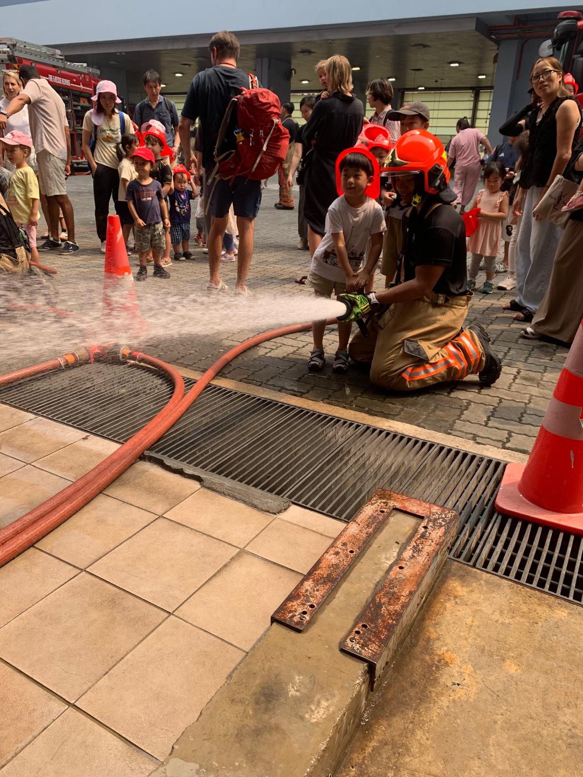 Child learning to use a fire hose with a firefighter